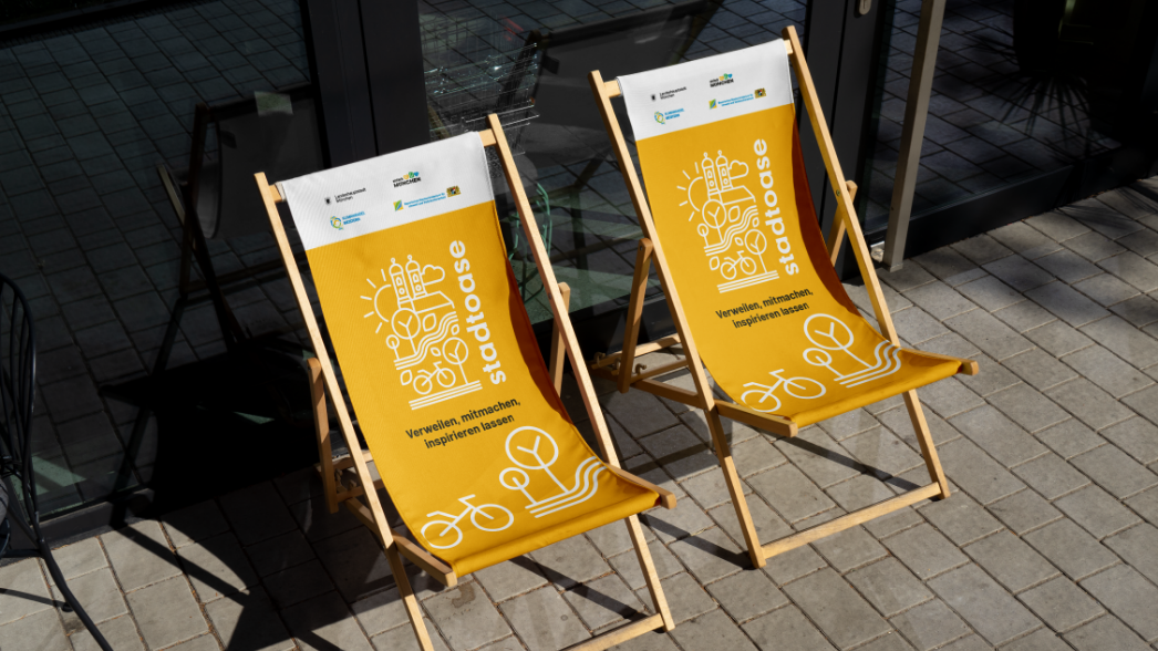 Event / öffentlicher Raum / Klimakommunikation - Raum für Klimaschutz und Mobilität Zwei gelbe Stadtoase-Liegestühle mit Logo, Slogan Verweilen, mitmachen, inspirieren lassen und Partnerlogos von München und klima.bayern