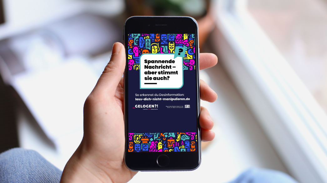 Smartphone mit Social-Media-Kampagnenmotiv: Sprechblase Spannende Nachricht – aber stimmt sie auch? und GELOGEN?!-Branding